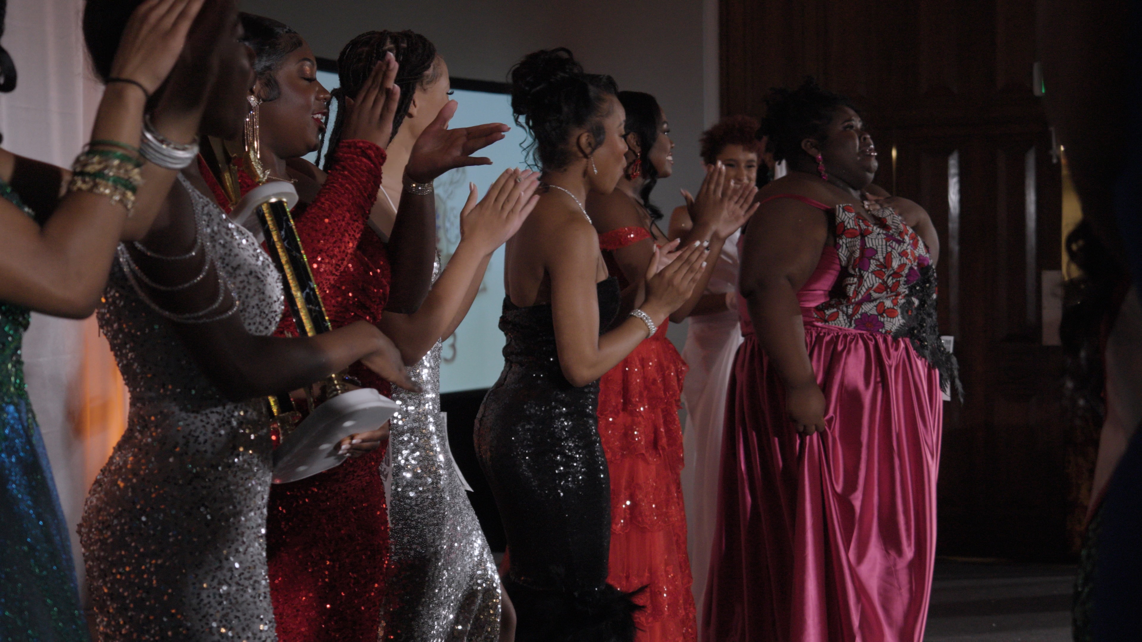Pageant contestants in formal gowns applauding on stage