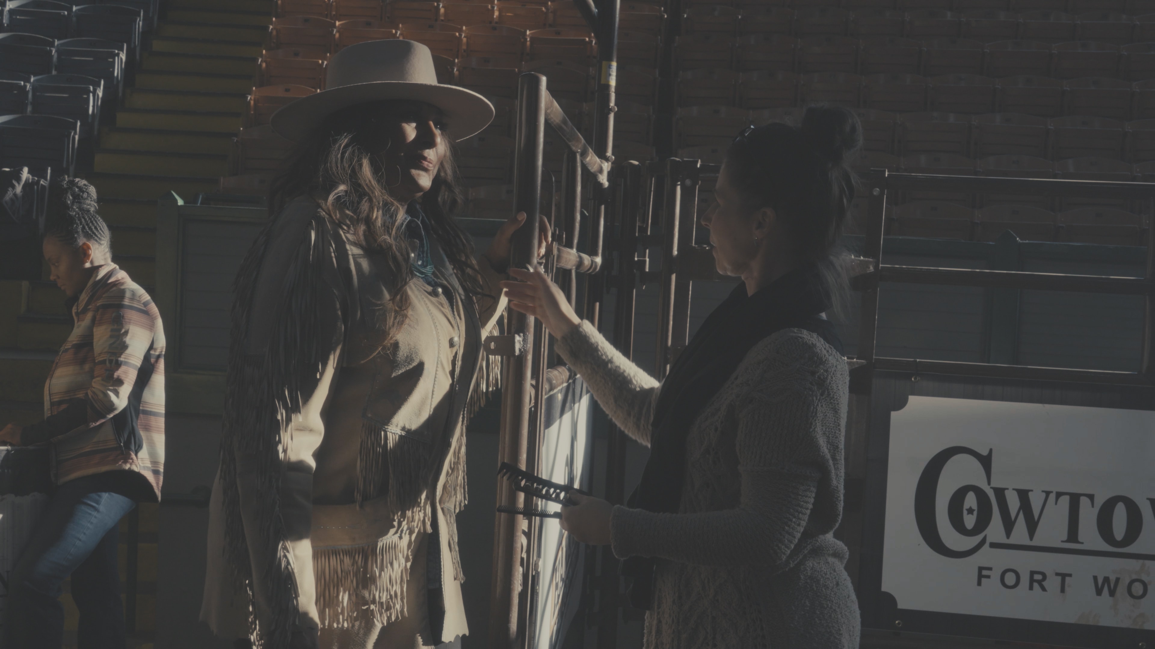 Woman in fringe jacket being prepped by crew member at Cowtown arena