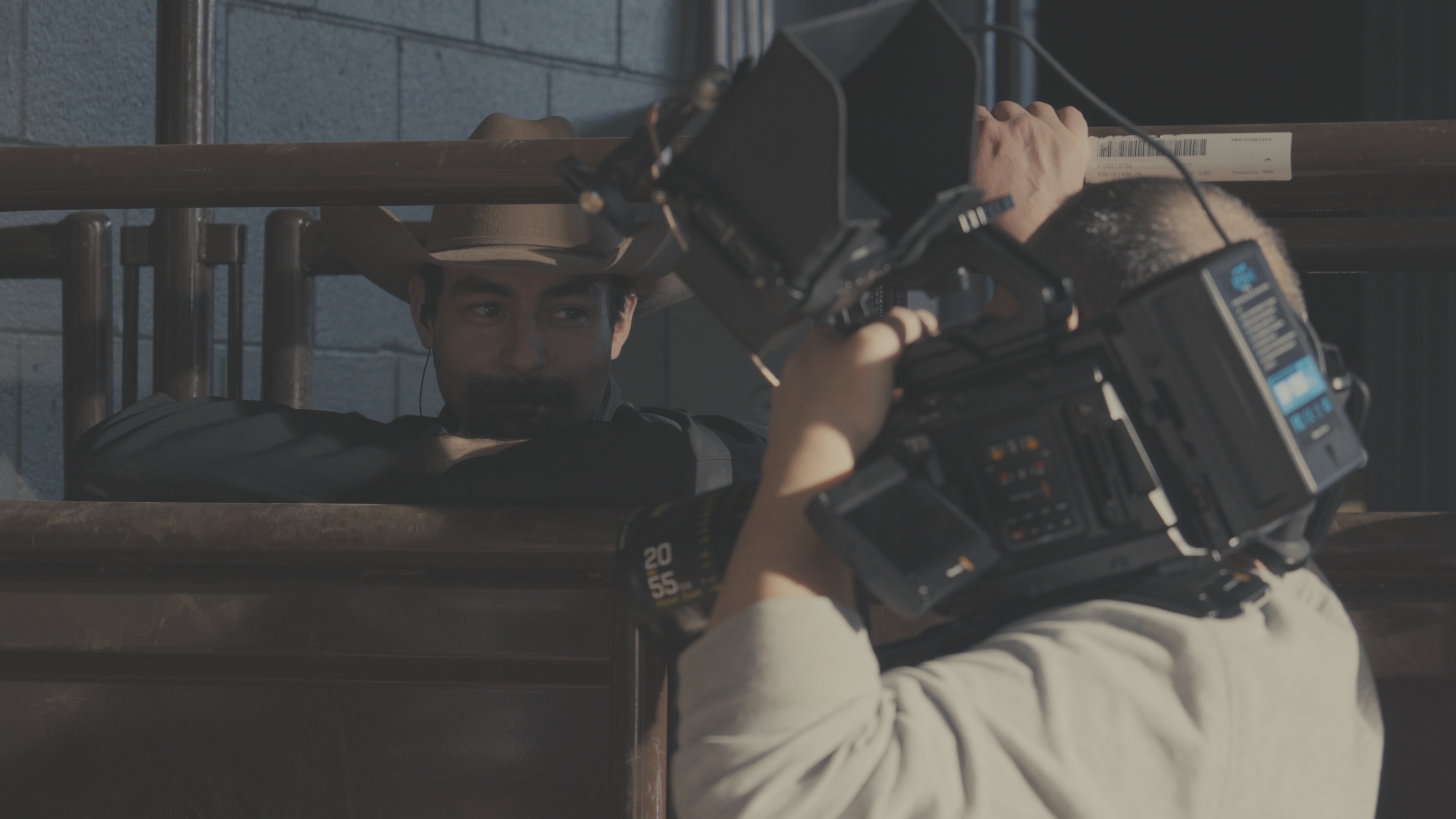Cinematographer filming actor in cowboy hat through arena railings