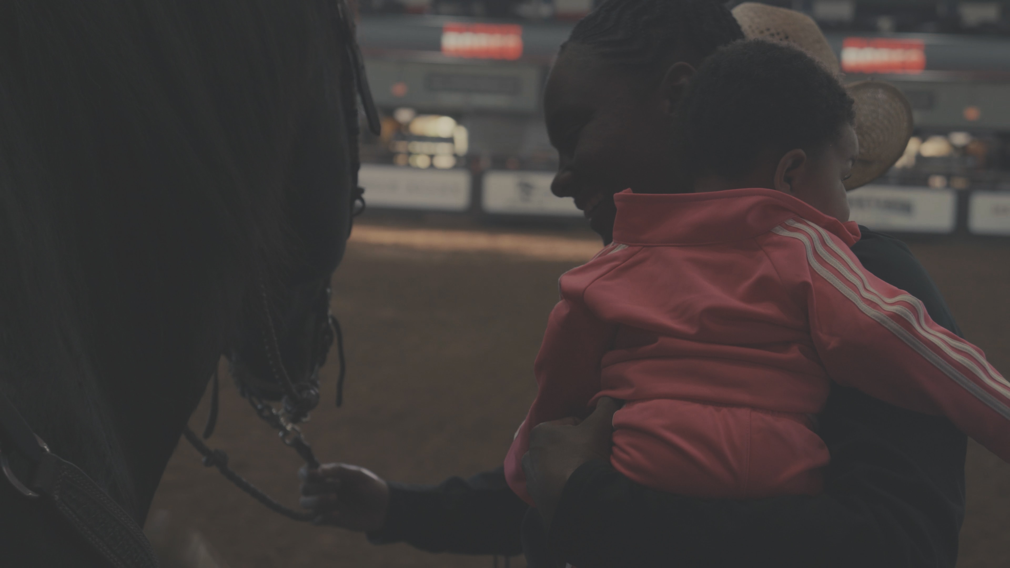 Child in red hoodie reaching up to touch a horse at the rodeo arena