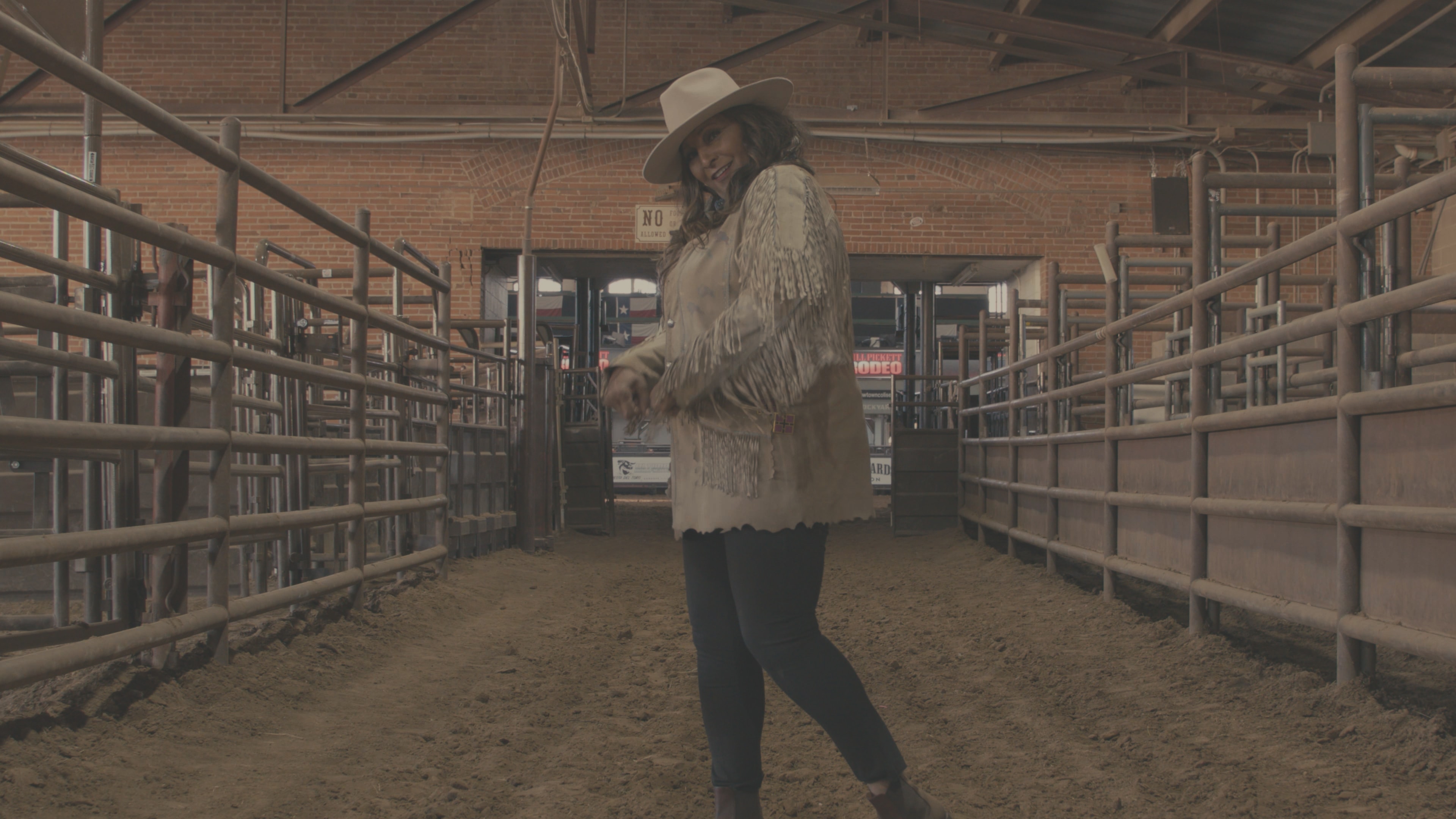 Woman in fringe jacket and cowboy hat walking through the Stockyards cattle pens