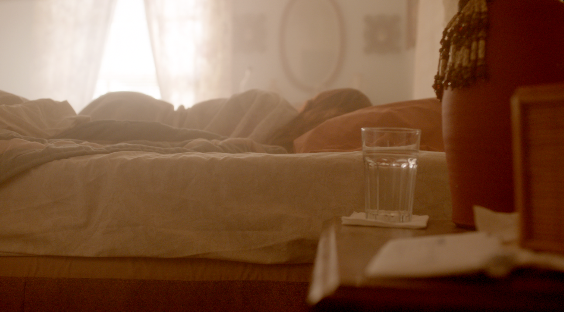 Warm cinematic bedroom scene with glass of water on nightstand