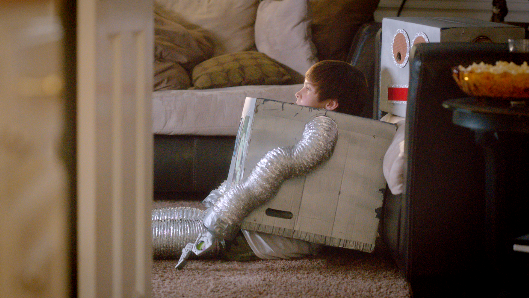Boy in homemade robot costume watching TV on living room floor