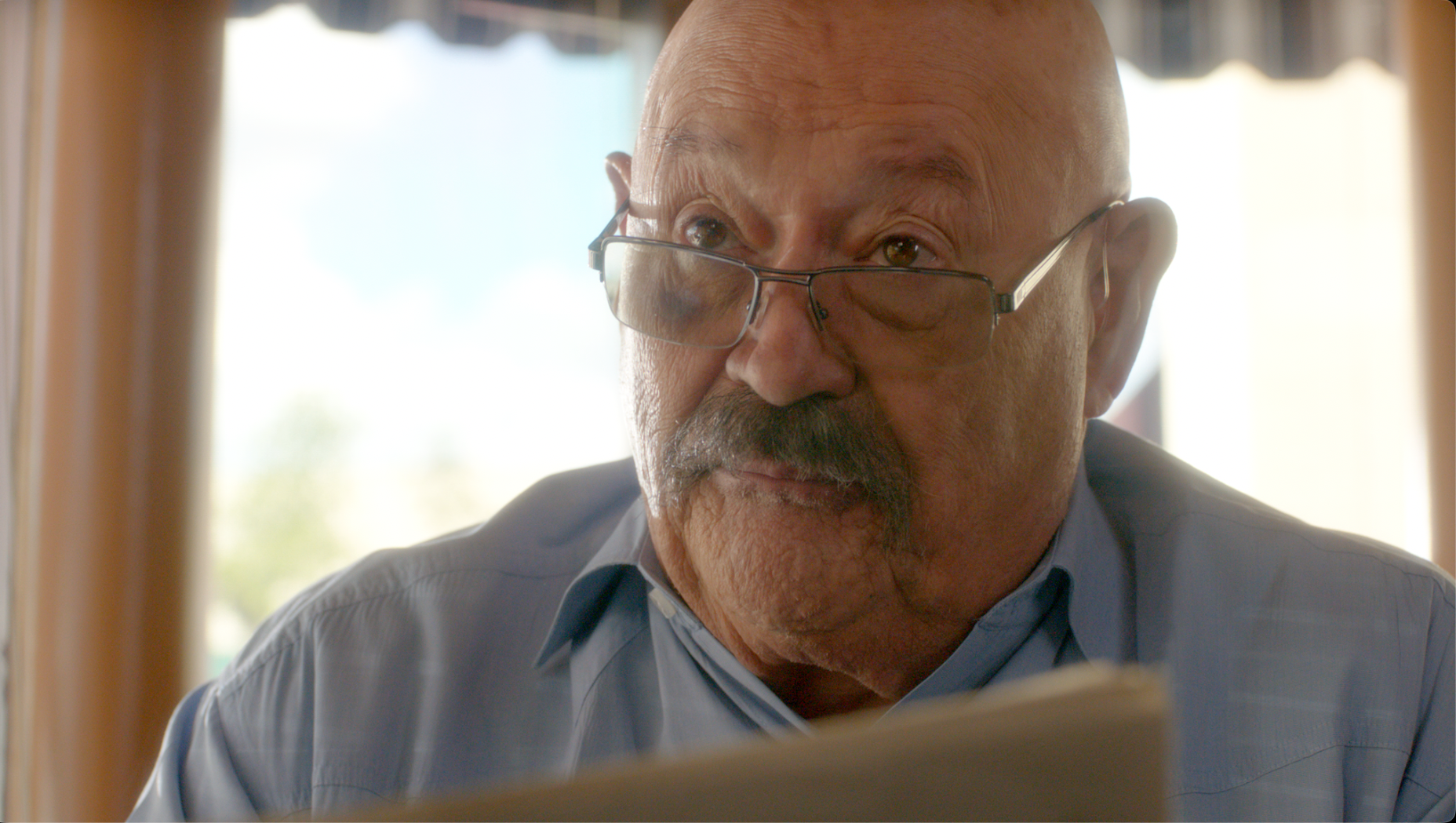 Older man with glasses reading a document in warm backlight