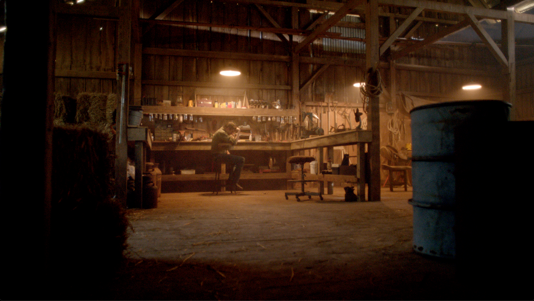 Man alone at workbench inside a warmly lit barn at night