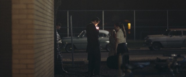 Group of teens gathered around a light in a dark parking lot at night