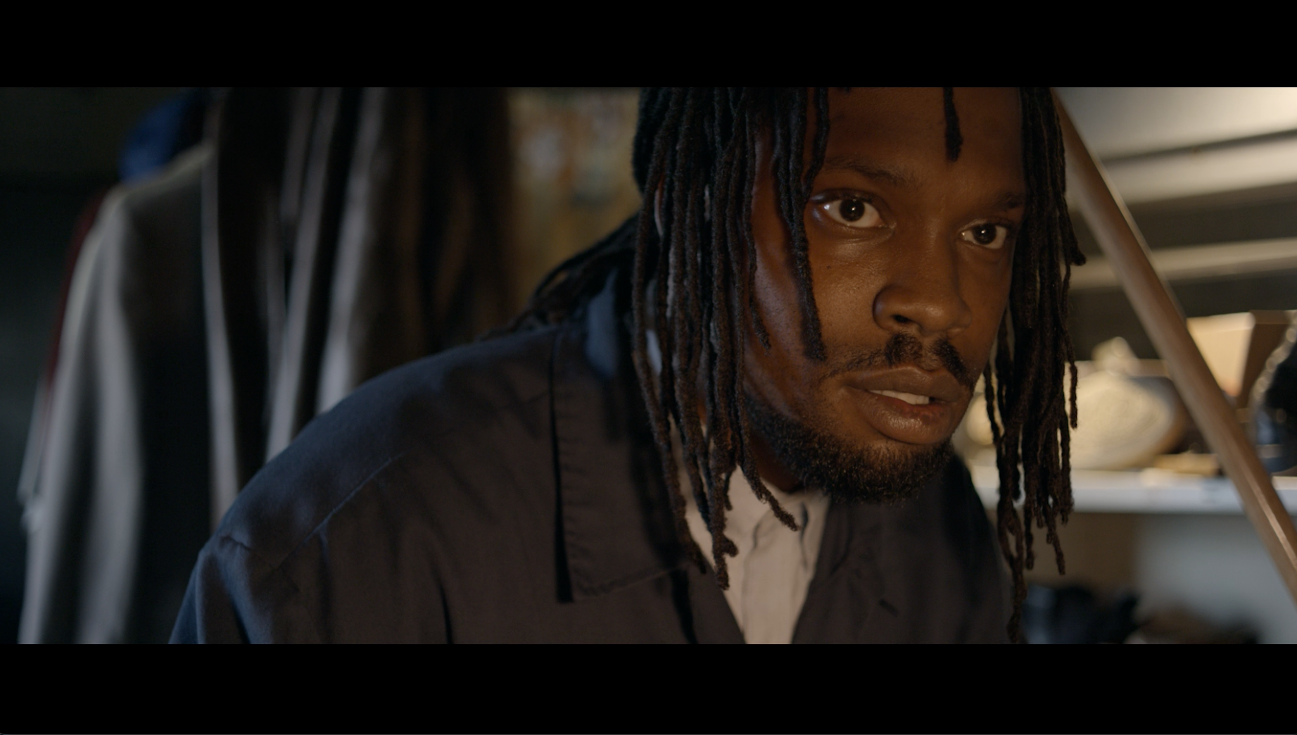 Man with dreadlocks looking intensely at camera in dark room