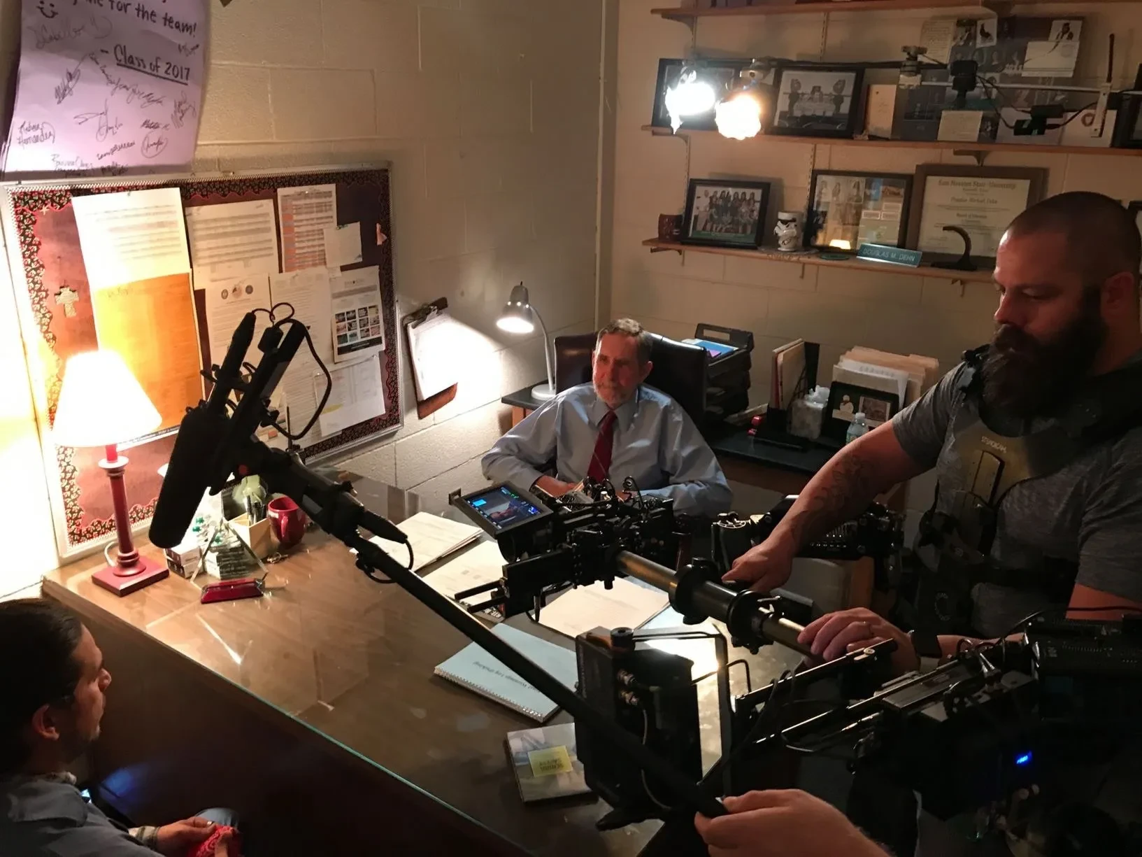 Camera crew filming interview subject at office desk