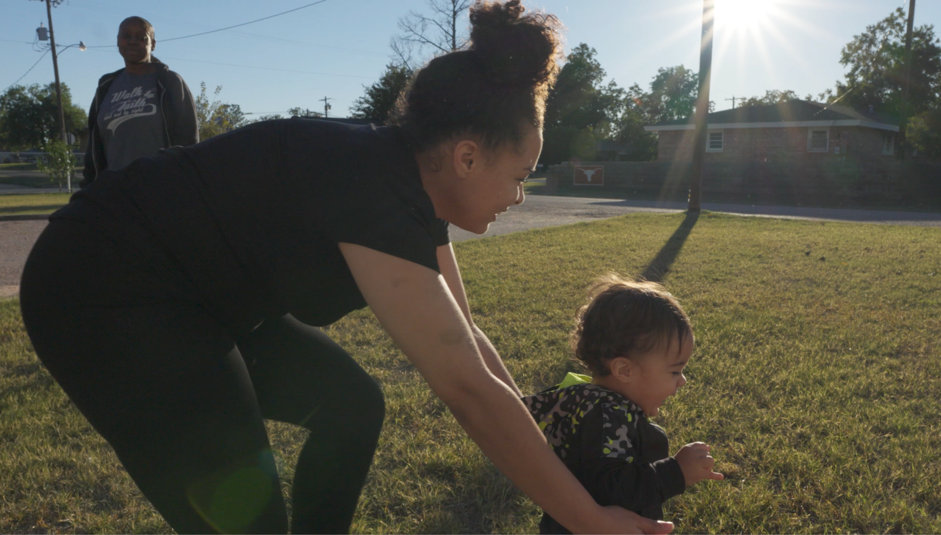 Mother and child playing on grass in golden sunlight