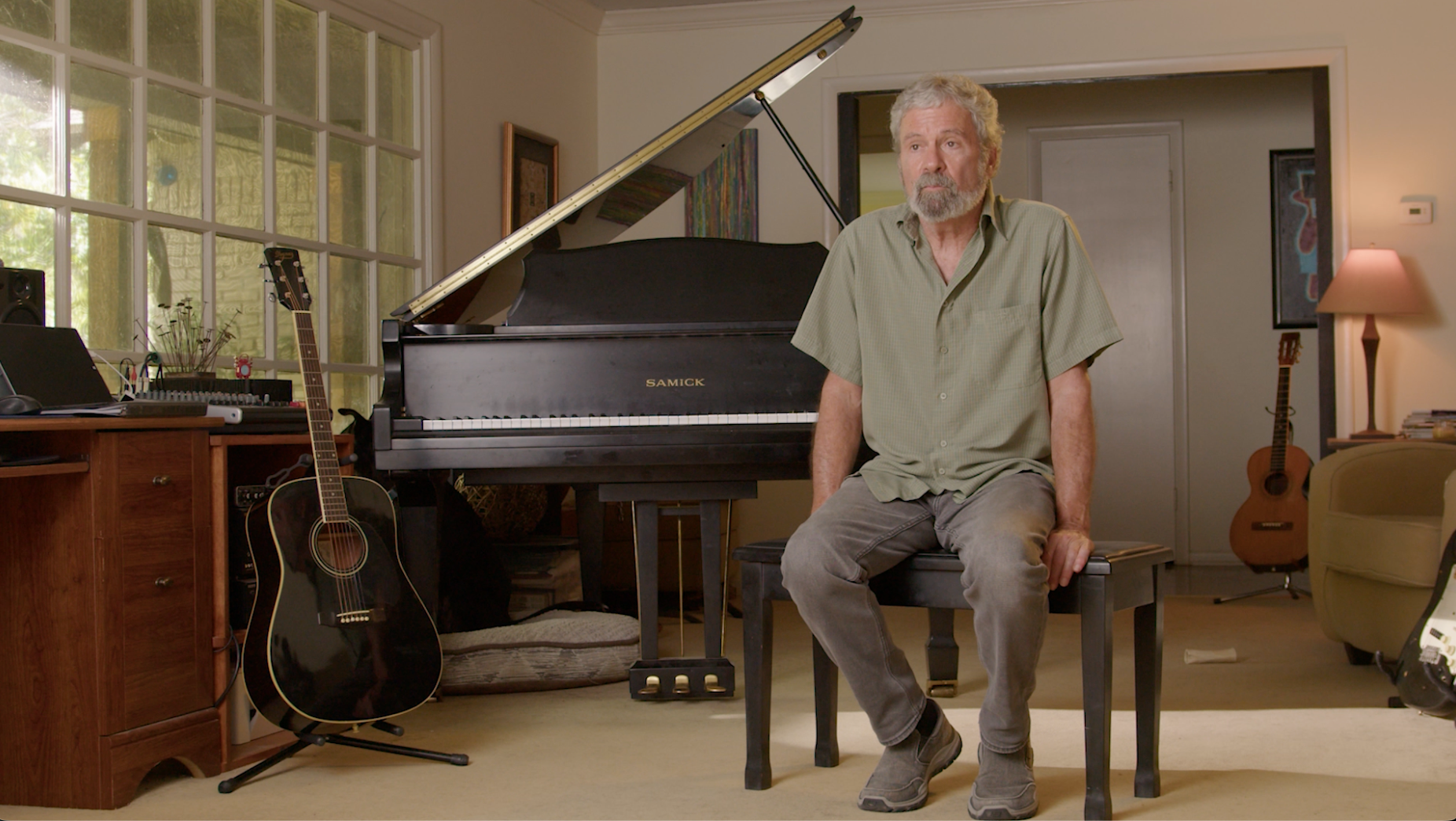 Musician seated at Samick grand piano surrounded by guitars